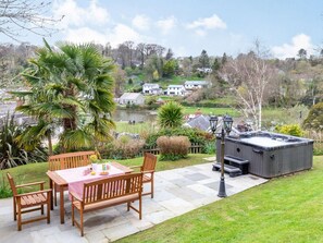 Eine Terrasse mit Tisch und Stühlen, einem Whirlpool und Blick auf einen See mit Häusern im Hintergrund.