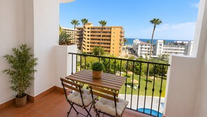 Ein Balkon mit Tisch, Stühlen, einer Topfpflanze und Blick auf ein Schwimmbecken und Gebäude.