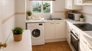 Eine kompakte Küche mit Waschmaschine, Mikrowelle, Backofen und einem Fenster mit Jalousien.