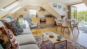 A loft-style living space with a kitchen, dining area, and a large window offering a view. - 2 Bed in Wedmore (oc-51339) (Middle Stoughton)