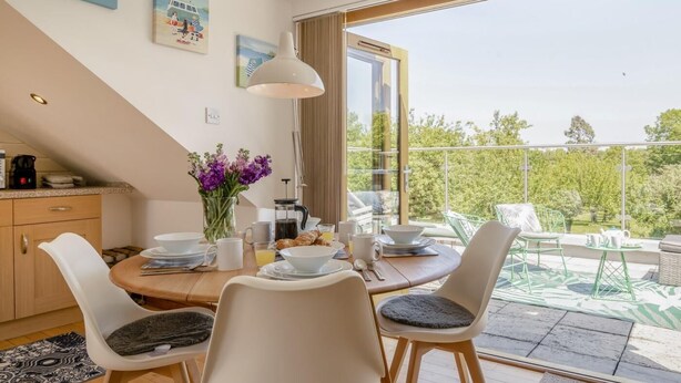 A dining area with a table set for four, a vase of flowers, and a view of greenery outside. - 2 Bed in Wedmore (oc-51339) (Middle Stoughton)