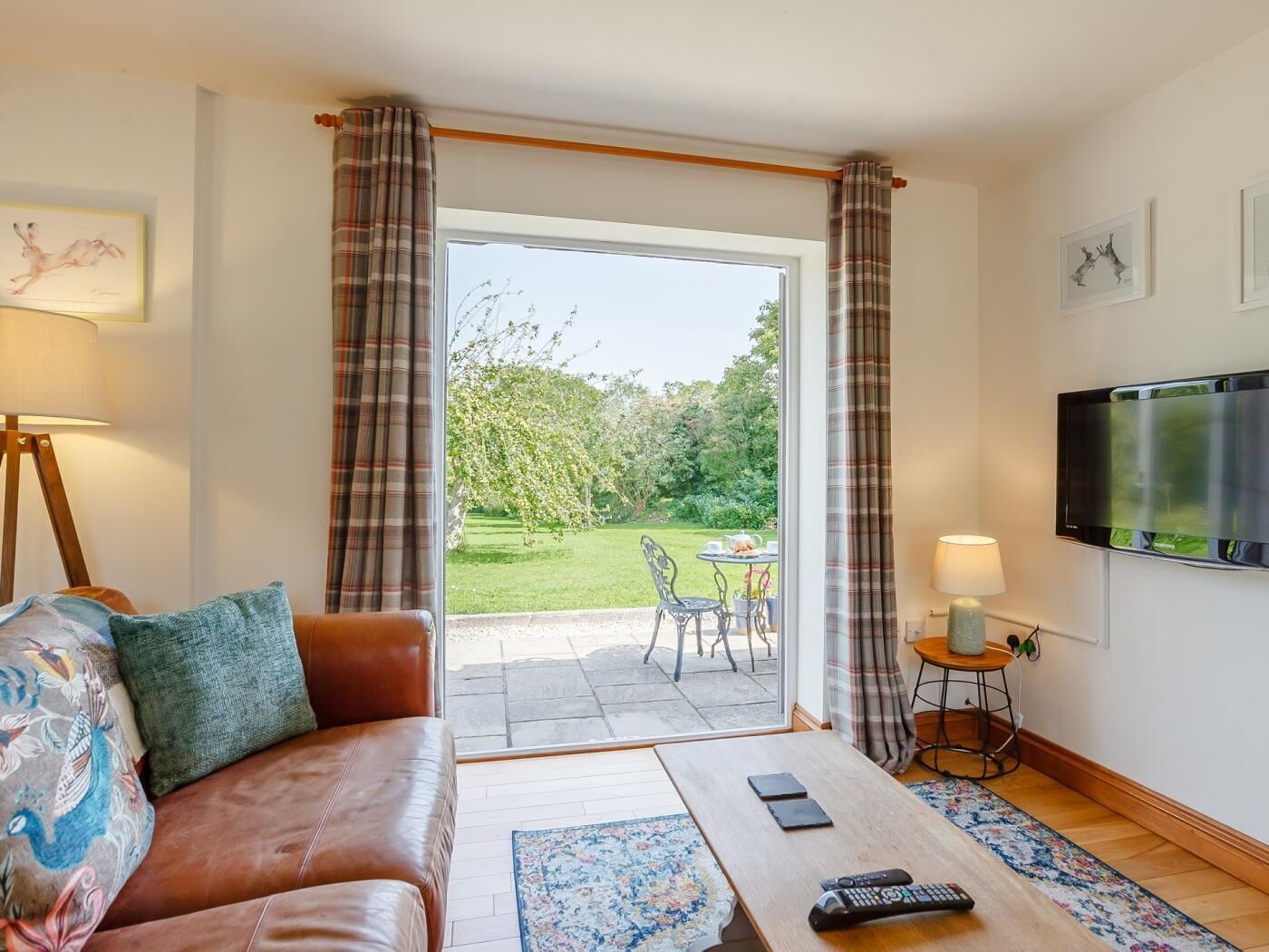A living room with a sofa, a coffee table, a TV, and a view of a garden through a glass door.