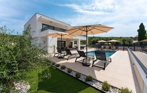 Ein modernes Haus mit Swimmingpool, Sitzgelegenheiten im Freien und einem gepflegten Garten.