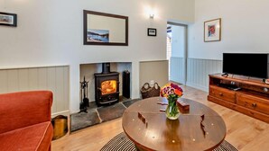 Ein Wohnzimmer mit Kamin, Fernseher, einem runden Holztisch und einem roten Sofa.
