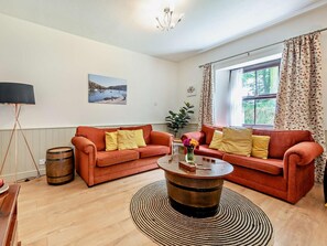 Ein Wohnzimmer mit zwei Sofas, einem Couchtisch, einer Lampe, einem Fass und einem Fenster mit Vorhängen.