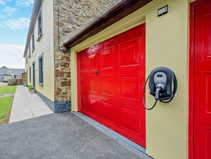 En byggnad med en röd garageport, en stenmur och en laddstation för elfordon av märket Zappi.