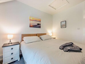 Ein Hotelzimmer mit einem Bett, zwei Nachttischlampen, einem Nachttisch, einem Wandbild und einem auf dem Bett gefalteten Handtuch.
