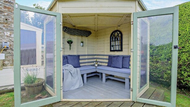 Ein gemütliches Holzpavillon mit einer Bank und einem kleinen Tisch, umgeben von einer Holzterrasse.
