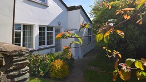 Een wit huis met een stenen muur, een tuin met verschillende planten en een heldere lucht.