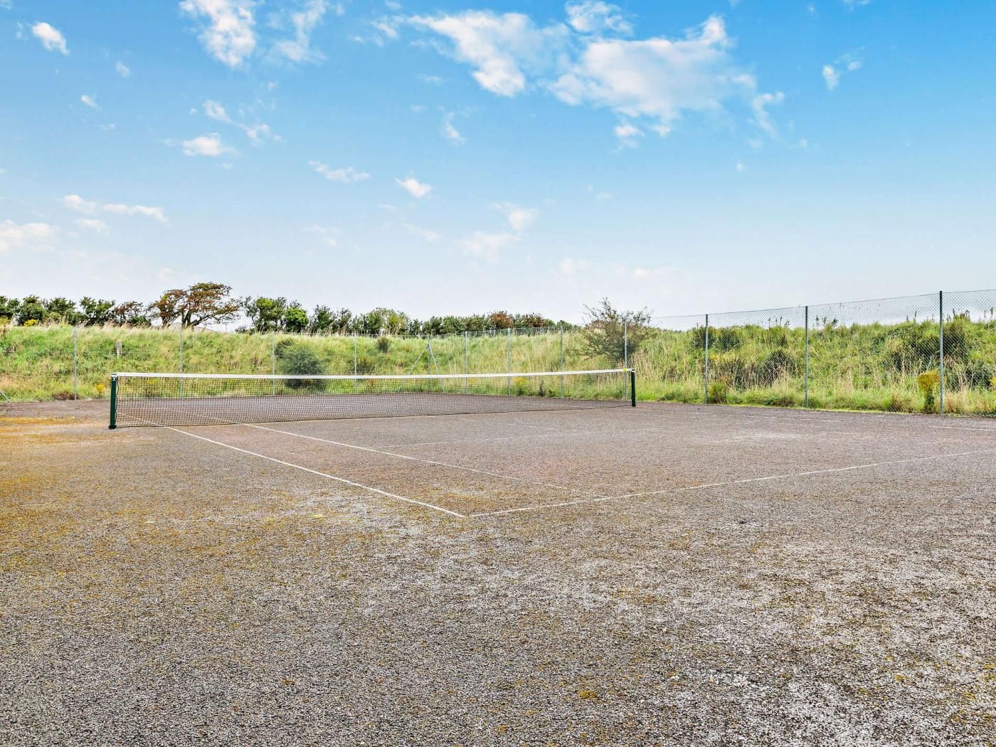 En udendørs tennisbane med net, omgivet af hegn og grønt.