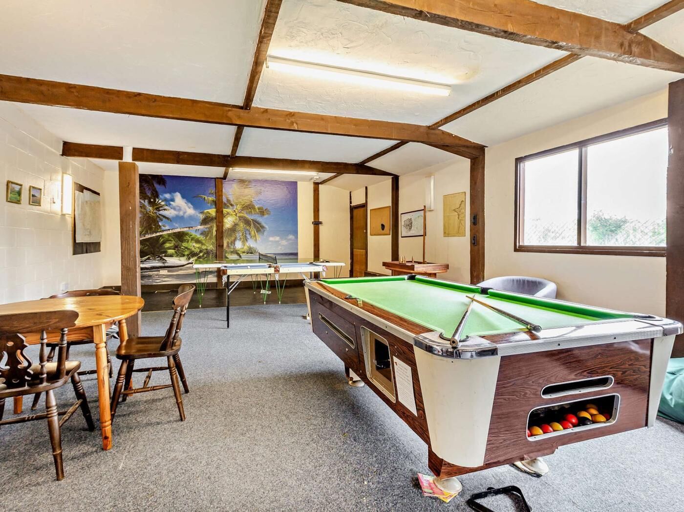 A pool table in a room with a view of palm trees, wooden chairs, and a table with a view.