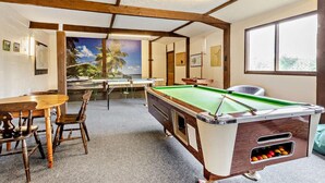 Een pooltafel in een ruimte met uitzicht op palmbomen, houten stoelen en een tafel.