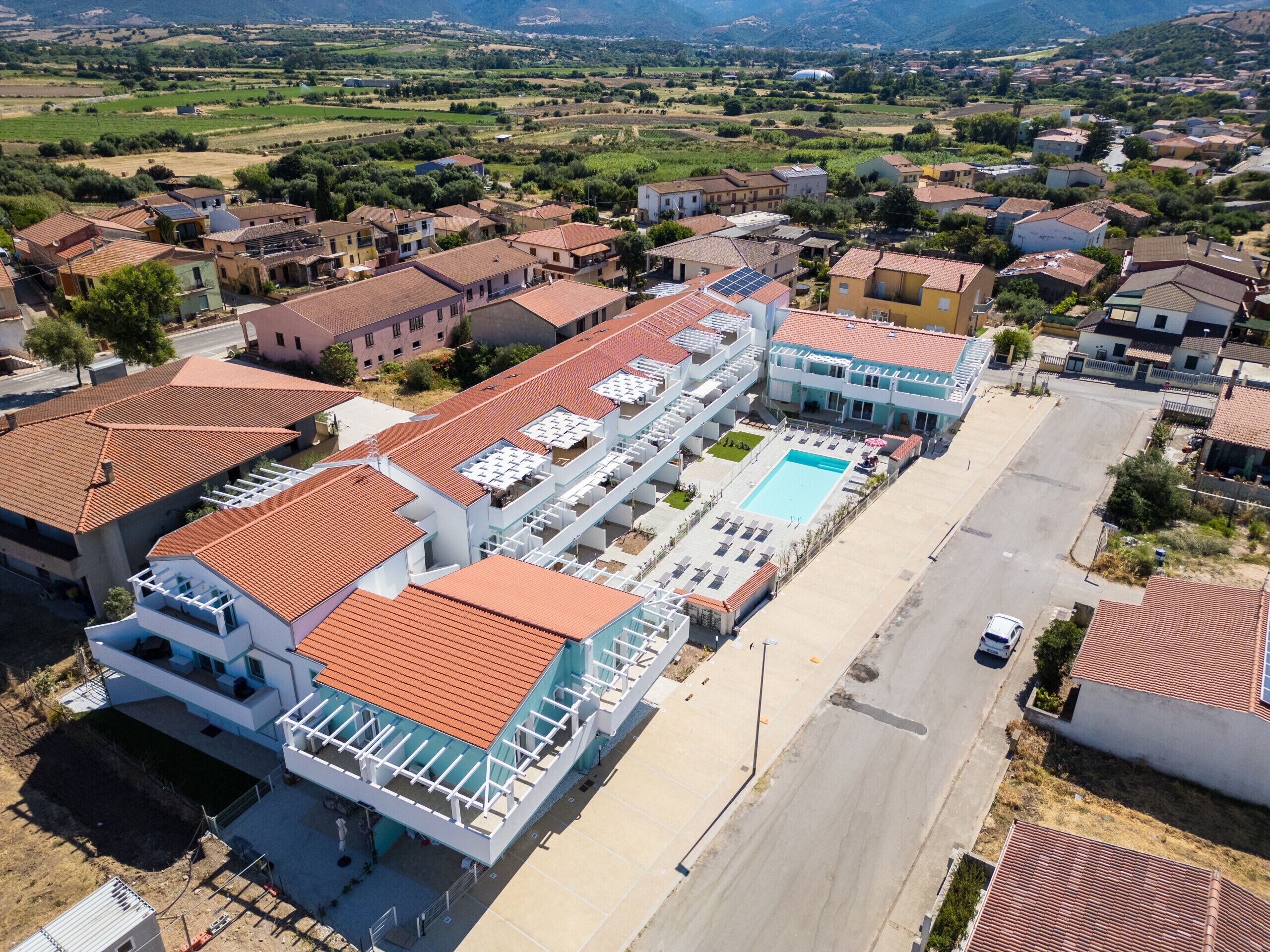 A large hotel with multiple floors, a swimming pool, and a parking area.