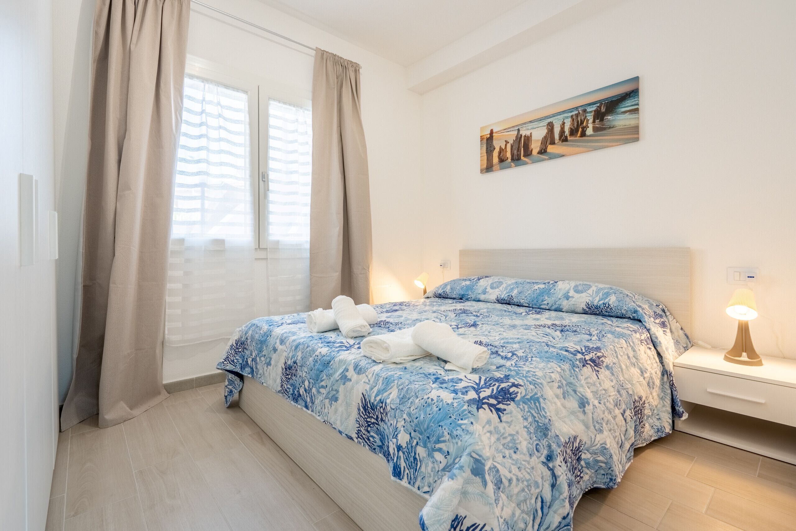 Une chambre à coucher avec un lit, des rideaux, un tableau, une lampe de chevet et une vue sur l’extérieur.