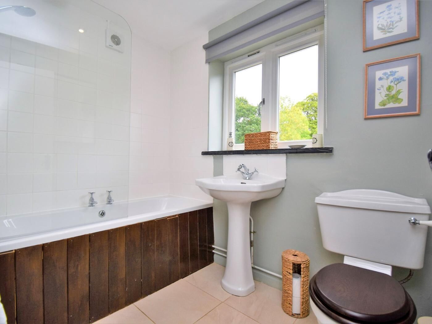 A bathroom with a bathtub, sink, toilet, and a window with a view of greenery.