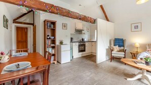 Un ambiente accogliente con un tavolo da pranzo in legno, una cucina con mobili bianchi e un soggiorno con divano e lampada.