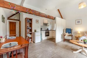 Ein gemütliches Interieur mit einem Holzesstisch, einer Küche mit weißen Schränken und einem Wohnbereich mit einer Couch und einer Lampe.