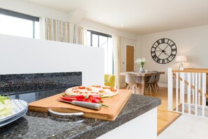 A modern kitchen with a wooden countertop, a pizza on a cutting board, and a dining area with chairs and a table. - 3 Bed in Bideford (oc-52079) (Westward Ho!)