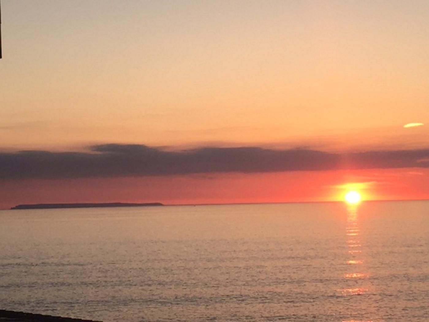A sunset over a calm sea with a distant landmass.
