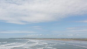 Eine Küstenlandschaft mit Strand, Meer und einer fernen Küstenlinie unter bewölktem Himmel.