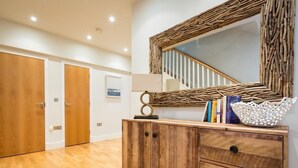 Ein Zimmer mit Holzboden, einem Holzkasten mit Schubladen, einem Spiegel mit gewebtem Rahmen, einer Treppe mit weißen Geländern und einem gerahmten Bild an der Wand.