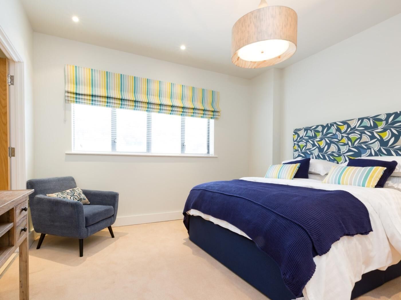 A bedroom with a bed, a chair, a window with blinds, and a ceiling light.