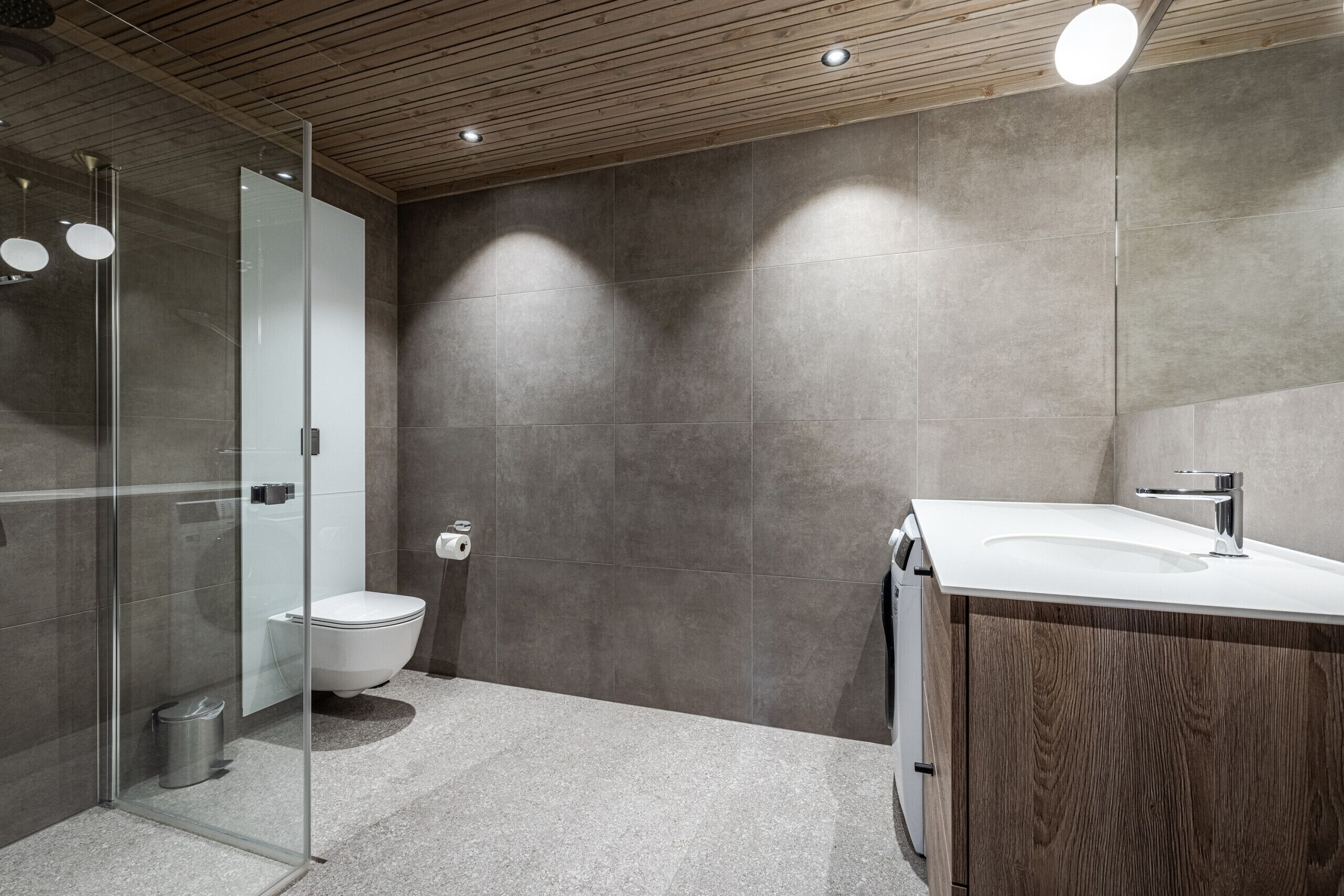 Et moderne badeværelse med en glasbrusekabine, et hvidt toilet og en trævaskebord med vask.