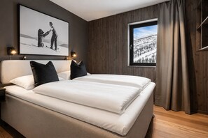 Ein Schlafzimmer mit einem Bett, einem gerahmten Bild an der Wand, einem Fenster mit Vorhängen und einem Holzboden.