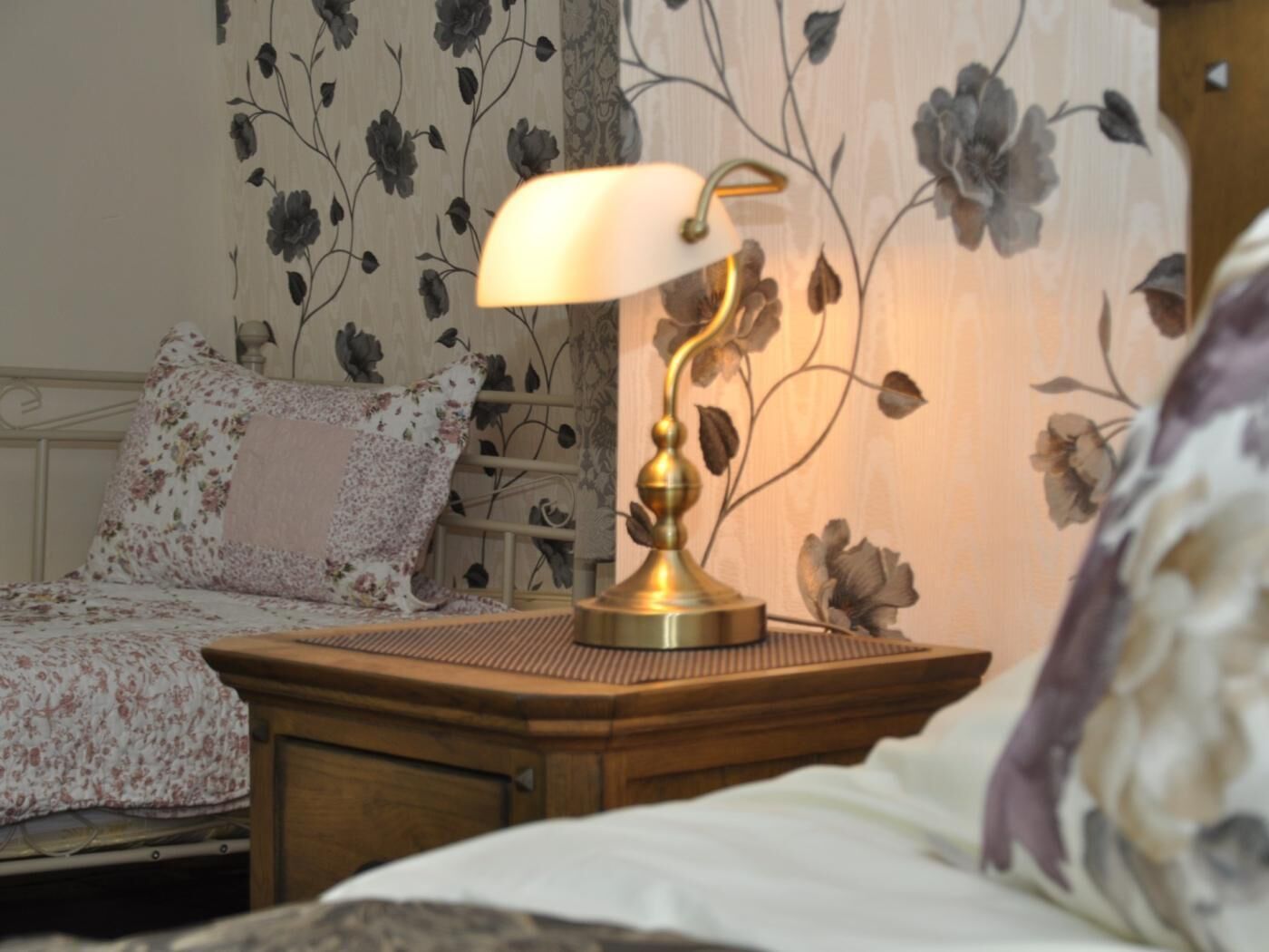 A bed with floral bedding, a bedside table with a lamp, and a wall with floral wallpaper.