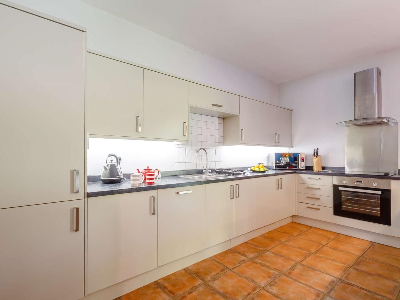 Een moderne keuken met witte kasten, een zwart aanrecht, een rvs-afzuigkap en een betegelde vloer.