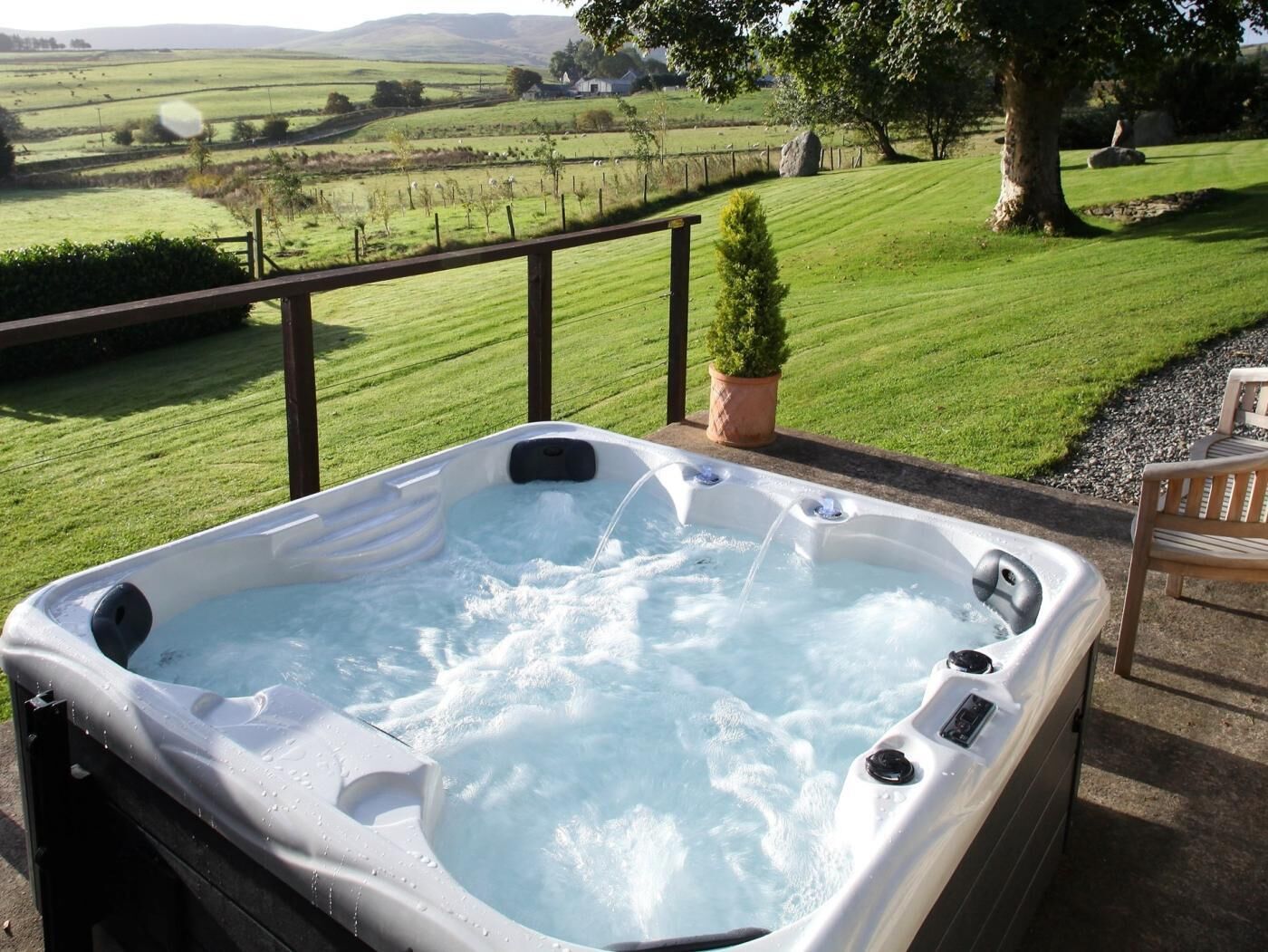 A hot tub with a view of a green landscape and a tree.