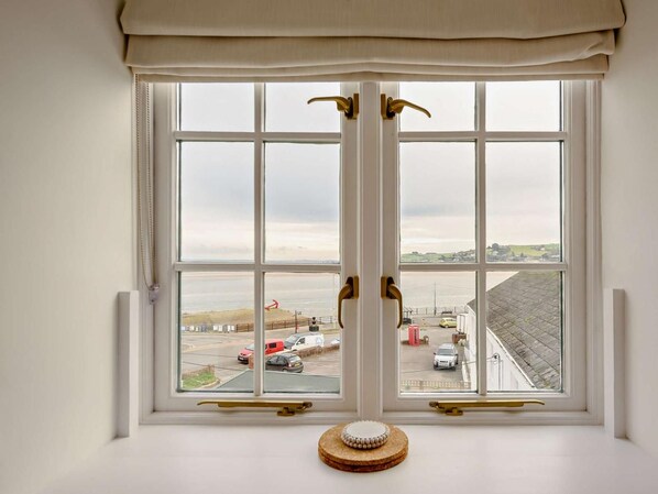 Ein Zimmer mit einem großen Fenster, das auf eine Küstenlandschaft blickt, mit Blick auf das Meer und einen Steg.