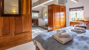Ein Schlafzimmer mit Holzschrank, Bett mit blauer Decke, Schreibtisch und Fenster.
