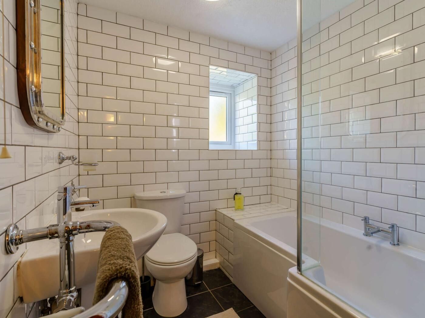 Et badeværelse med hvide metrofliser, toilet, vask, badekar og en brusekabine i glas.