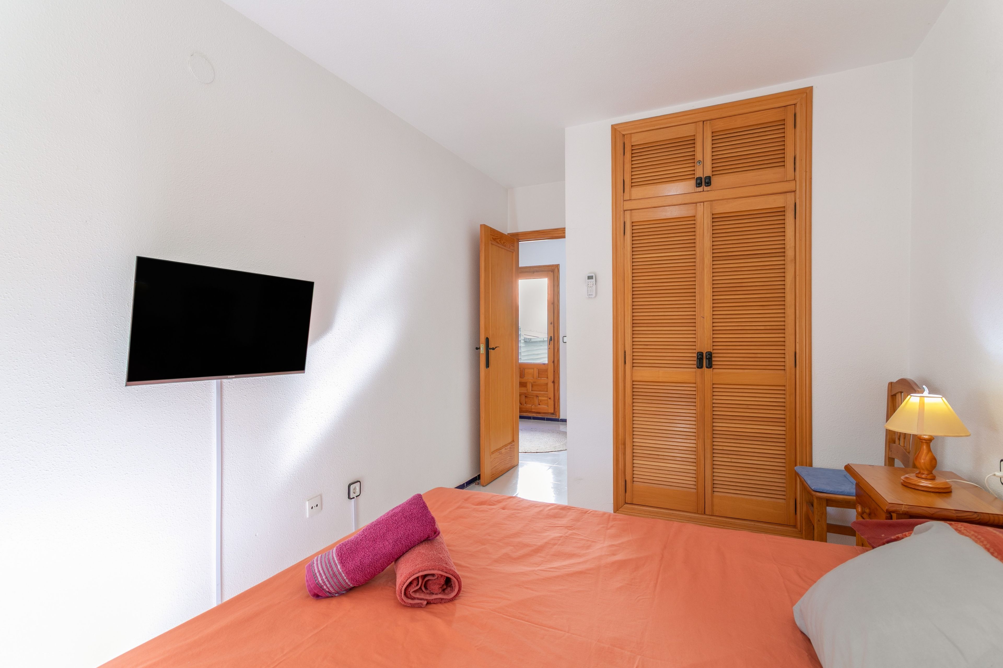 Een hotelkamer met een bed, een aan de muur bevestigde televisie, een houten kledingkast, een nachtkastje met een lamp en een stoel.