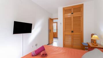 Een hotelkamer met een bed, een aan de muur bevestigde televisie, een houten kledingkast, een nachtkastje met een lamp en een stoel.