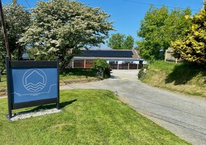 A residential area with a house, a paved driveway, and a sign with a water wave symbol. - 1 Bed in Bude (oc-53410) (Crackington)