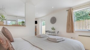 Ein Schlafzimmer mit einem großen Bett, einem kleinen Tisch, einem Stuhl, einem Fenster mit Vorhängen und einer Wanduhr.