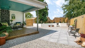 Ein überdachter Patio-Bereich mit Sitzgelegenheit, Grill und Holzzaun.