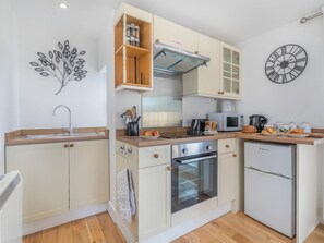 A modern kitchen with a microwave, oven, and refrigerator. There is a wooden cabinet with a 'NO SMOKING' sign above it. A wall clock and a decorative branch are also visible. - 1 Bed in Bude (oc-53410) (Crackington)