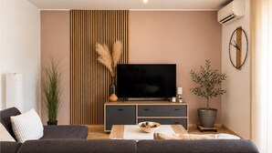 A modern living room with a sofa, a TV on a wooden stand, a potted plant, and a wall-mounted air conditioner. - Beautiful home in Pula (Pula)