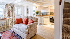 A cozy living room with a sofa, a dining table, and a kitchen in the background.