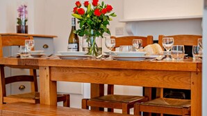 A wooden dining table with a vase of red roses, plates, and glasses set for a meal. - 3 Bed in Newquay (oc-53688) (Newquay)