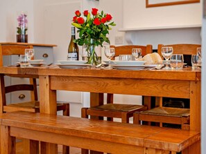 Ein Holztisch mit einer Rosenvase, Tellern und Gläsern, gedeckt für eine Mahlzeit.