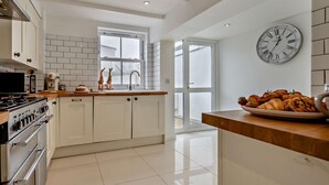 A modern kitchen with white cabinetry, a stainless steel stove, and a large window. - 3 Bed in Newquay (oc-53688) (Newquay)