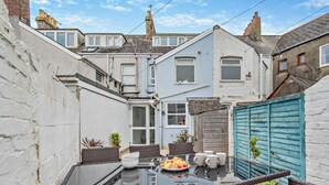 A rooftop patio with a glass table, wicker chairs, and a blue fence. - 3 Bed in Newquay (oc-53688) (Newquay)