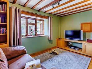 A living room with a sofa, a TV, a bookshelf, a window with curtains, and a wooden ceiling.