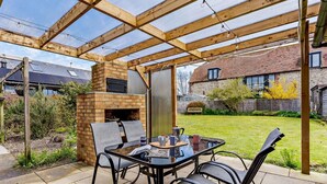 Une terrasse couverte avec un four en briques, une table avec des chaises et, en arrière-plan, une maison en briques.