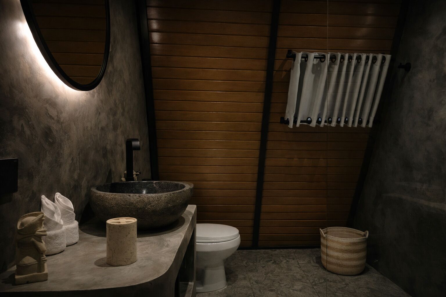 A modern bathroom with a stone sink, toilet, and a towel rack.