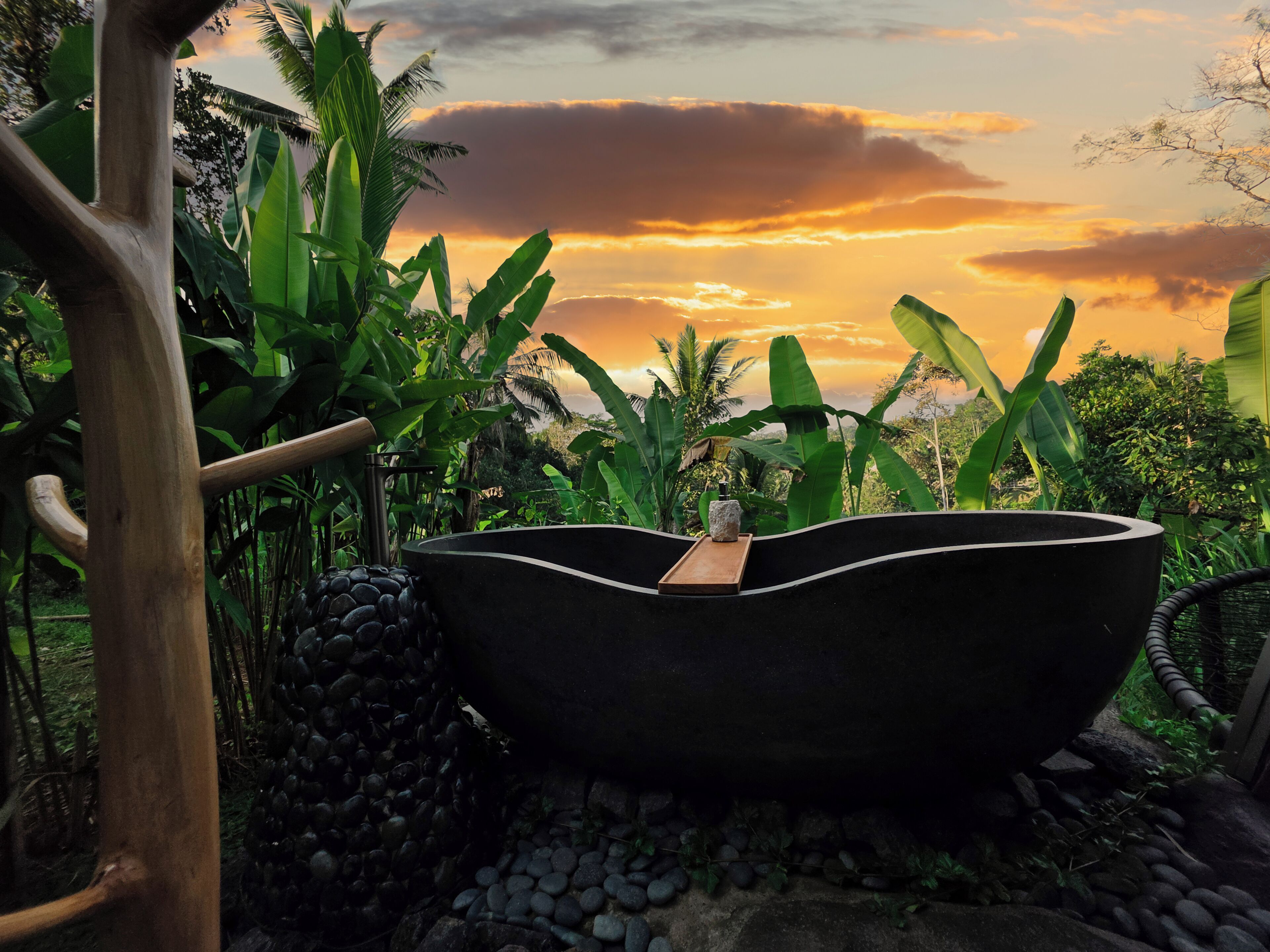 Una bañera negra grande rodeada de exuberante vegetación y una estructura de madera.
